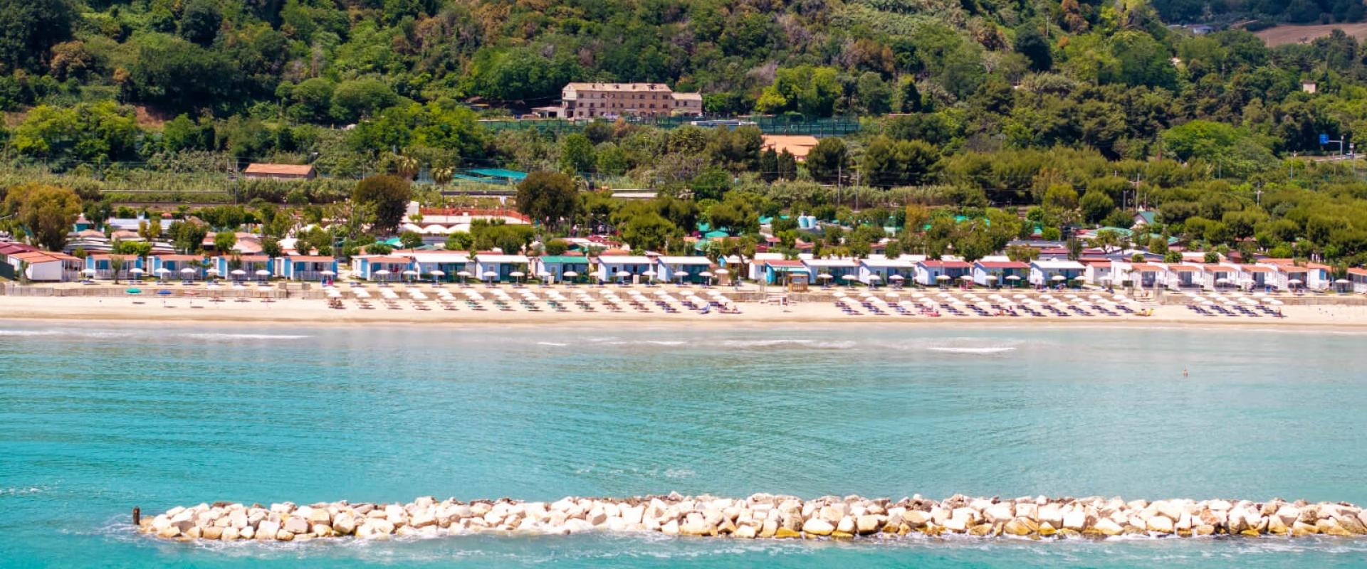 Strand mit Sonnenschirmen und grünen Hügeln im Hintergrund.