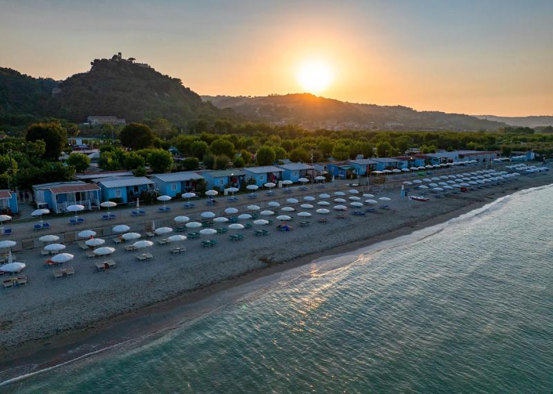 Strand bei Sonnenuntergang mit Sonnenschirmen und Hütten im Hintergrund.